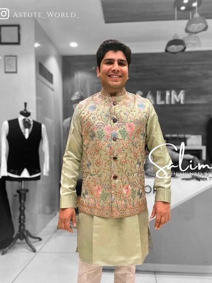 A client smiling in a light green kurta set with a matching Nehru jacket. The jacket is adorned with colorful floral embroidery, perfect for a daytime event.