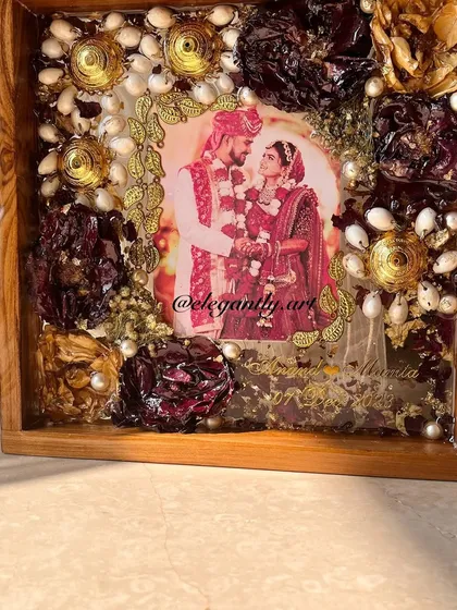 A close-up of a teakwood frame filled with preserved kaleera and varmala flowers. The sunlight catches the details, showing the beautiful texture and color of the preserved items.
