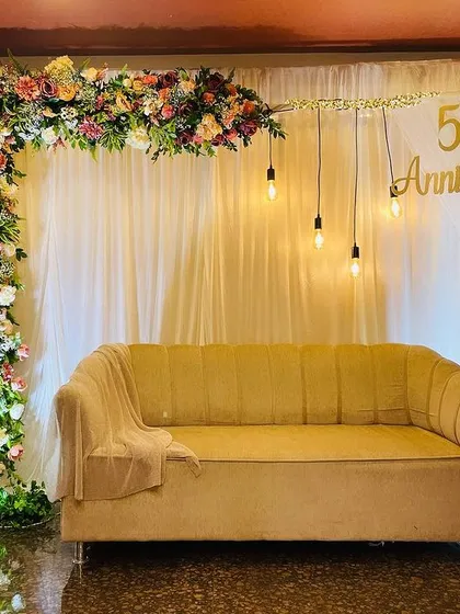 Celebrating 50 years of togetherness with this elegant and minimalist anniversary decor. We created a beautiful photo corner with a lush floral arch, draped curtains, and warm Edison bulb lighting to provide a sophisticated backdrop for this golden milestone.