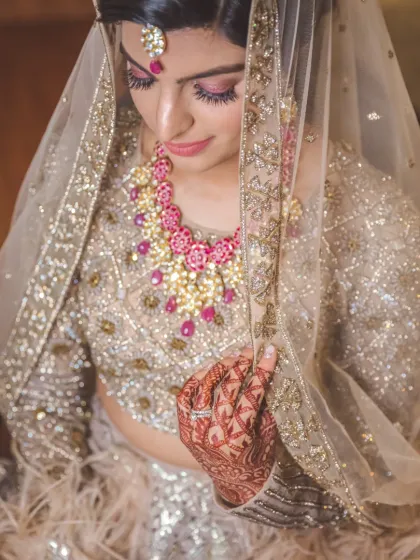 A delicate and graceful portrait of a bride looking down, her face partially veiled, highlighting her intricate jewelry and makeup.