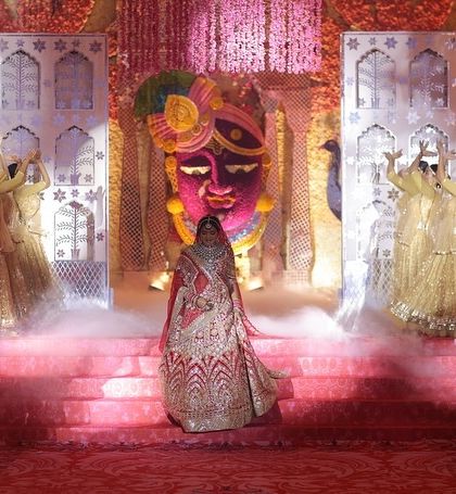 The bride's grand entry for a royal-themed Jaimala. We used professional dancers in golden attire and dramatic smoke to create a divine atmosphere as she walked towards the stage, which featured a massive, ornate floral mask prop.