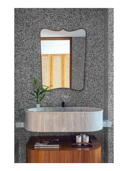 A bathroom featuring a custom floating vanity with a marble sink. The capsule shape of the sink and the curved mirror above create a soft, organic feel against the textured terrazzo wall.