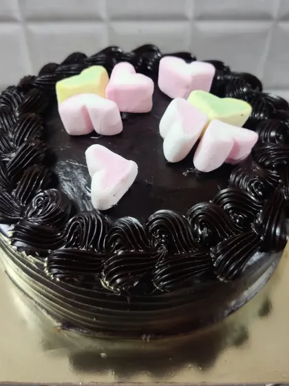 A simple yet sweet chocolate cake decorated for someone special. The top is adorned with colorful heart-shaped marshmallows, and the sides feature a border of rich chocolate frosting swirls.