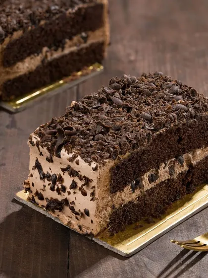 A slice of rich chocolate pastry, styled with dramatic side lighting to highlight its layers. This moody shot creates a sense of indulgence and premium quality.