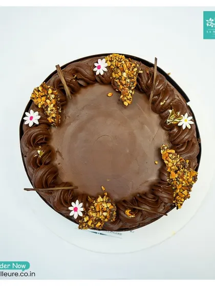 A top-down view of the Chocolate Almond Nougatine cake, showing the placement of the crunchy nougatine clusters and edible flowers.