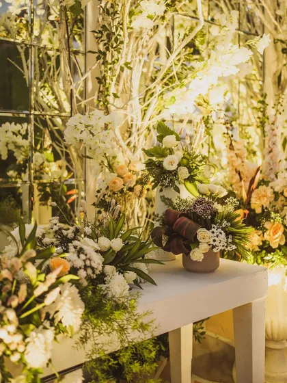 A beautiful detail shot of the floral arrangements at a white-themed wedding. The mix of white branches, fresh flowers, and warm lighting creates a sophisticated and inviting atmosphere.