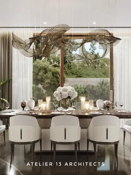 In this farmhouse dining room, a fluidic Italian metal and glass chandelier hangs above a veneer-top table with a fluted leather base. We used bronze Armani marble for the flooring and surrounded the space with beige Italian chairs to create a warm, opulent setting for gatherings.