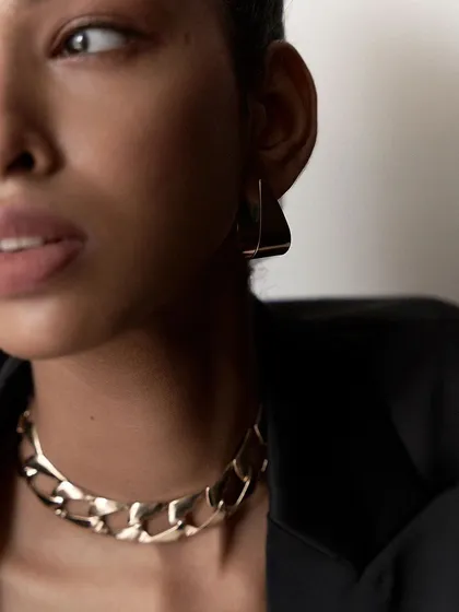 A close-up, moody portrait focusing on jewelry and expression. The tight crop and soft lighting create an intimate and mysterious feel, perfect for editorial use.