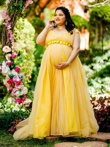 This image highlights the delicate floral belt detail on the yellow empire-waist gown, a small touch that adds to the overall charm of the maternity look.