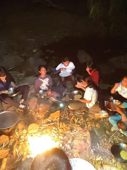 Campers gather around a campfire at night to cook their own meal, a key survival skill we teach.