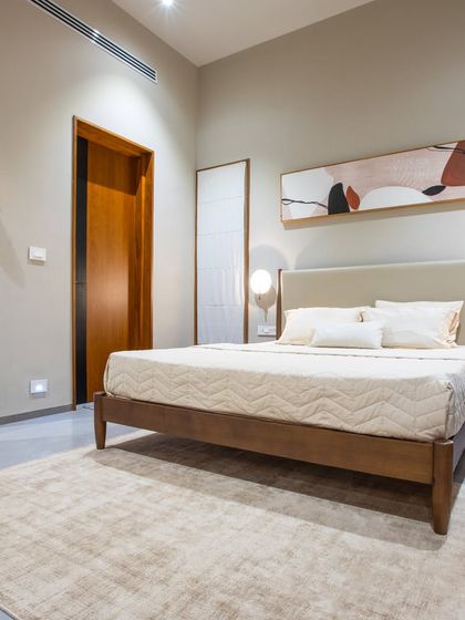 This guest bedroom is a picture of serene simplicity. A classic wooden bed frame is set against a neutral wall with elegant sconce lighting, while a large mirror enhances the sense of space and light.
