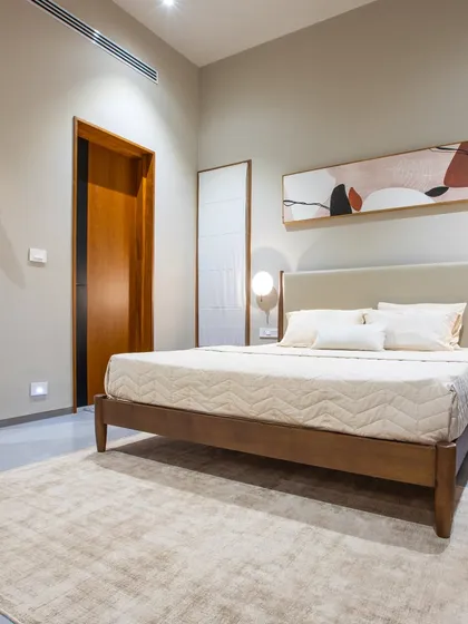 This guest bedroom is a picture of serene simplicity. A classic wooden bed frame is set against a neutral wall with elegant sconce lighting, while a large mirror enhances the sense of space and light.