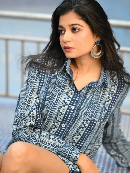 A portrait of a model in a blue printed shirt dress, taken for Sananda magazine. Her thoughtful expression and the casual styling make for a relatable and chic image.