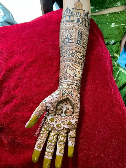 A full hand view showing the Taj Mahal motif on the forearm, connected to a traditional peacock design on the palm. The couple's initials 'S' and 'D' are also included.