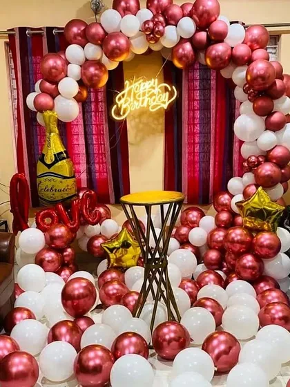 A vibrant birthday arch in metallic red and white, with a champagne bottle foil balloon and a 'Love' balloon for a celebratory feel.