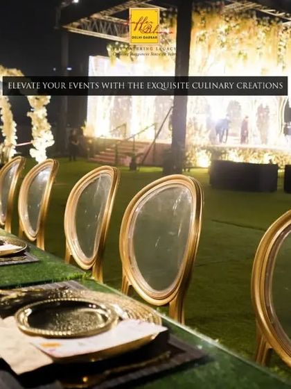 We elevate your events with exquisite culinary creations and stunning decor. This outdoor evening setup features a long dining table with elegant gold-accented chairs, overlooking a grand, beautifully lit stage.