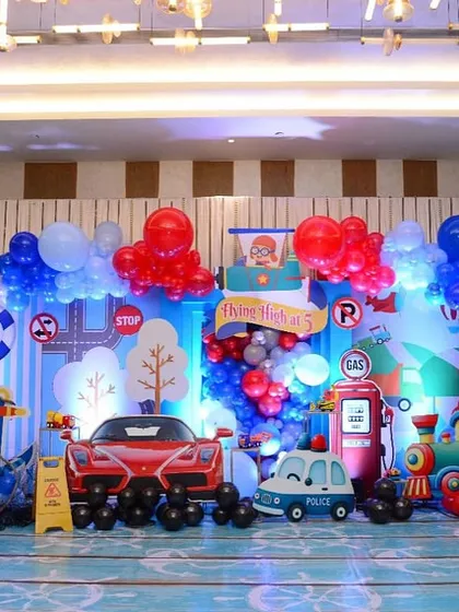 For Luv and Kussh's birthday, we created a world of travel. This main backdrop combined land, air, and sea transport themes with a Ferrari cutout, a gas station, a train, and an airplane, making it a grand stage for their adventure.