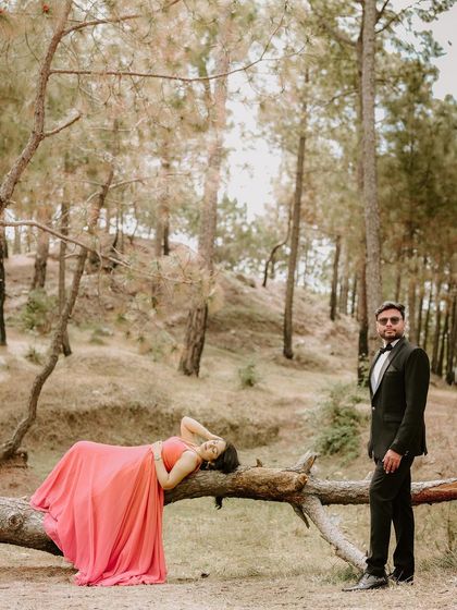 An artistic, posed shot with the bride-to-be reclining on a fallen log while her partner stands watchfully, creating a high-fashion look in a natural environment.