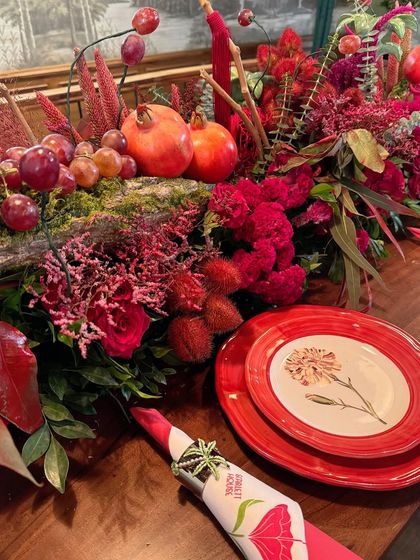 This place setting combines a floral-printed plate with a custom napkin and a rich backdrop of pomegranates, grapes, and red flowers from the table runner.