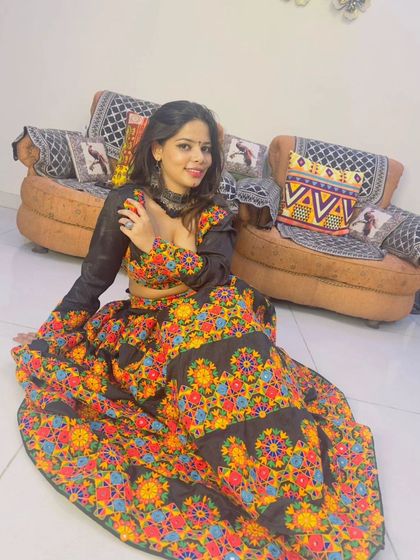 A model seated in a black chaniya choli with vibrant, multi-colored embroidery. The oxidized choker completes this festive look.