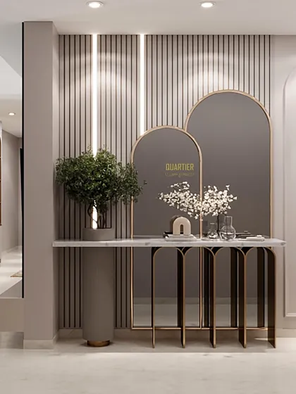 The foyer design for Apex D'Rio features a console table with a metallic frame and stone top, set against a wall of grey louvers. Arched mirrors and elegant wall lamps complete this sophisticated entryway.