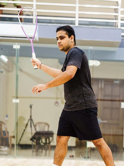Poised and balanced, Yash Salunkhe prepares to receive a serve. The glass wall of the court provides a clean backdrop, keeping the focus entirely on the athlete's ready stance.