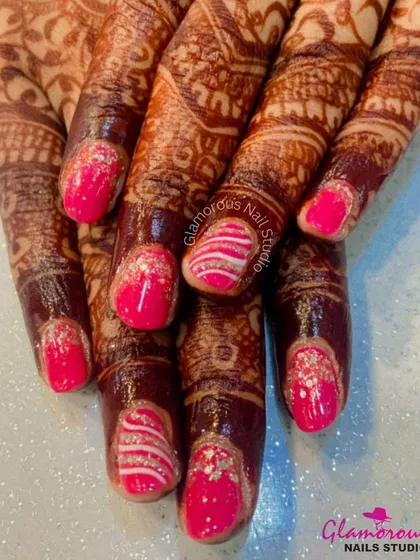 For the bride who loves a pop of color. This set features bright pink nails with silver glitter accents and intricate white swirl patterns, designed to stand out alongside traditional mehendi.