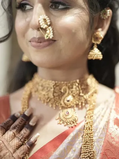 A close-up shot focusing on the bride's traditional nose ring and necklace, with her detailed mehendi visible on her fingertips.