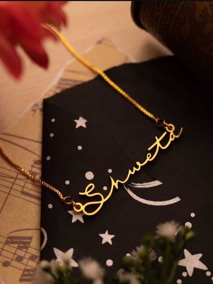 A 'Shweta' script necklace styled in a flat lay with floral and celestial elements. This shows the artistic and personal nature of my custom jewelry.