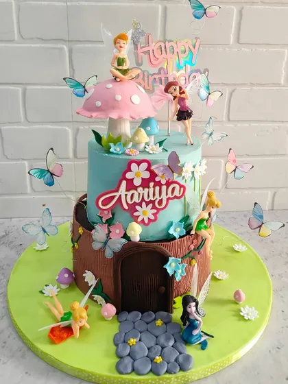 A closer look at our fairy garden cake. This two-tier cake features a whimsical fairy house design, complete with a fondant door, a mushroom on top, and tiny, delicate butterflies.