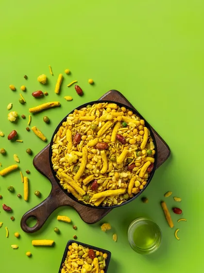 A top-down shot of Navratan Mixture for Sartaj Sweets & Namkeen. The vibrant green background and scattered ingredients create a dynamic, eye-catching image designed for modern snack packaging and e-commerce listings.