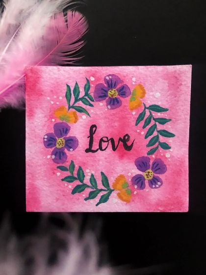 The finished "Love" floral wreath painting. The pink watercolor background and vibrant flowers make this a sweet and heartfelt piece of mini art.