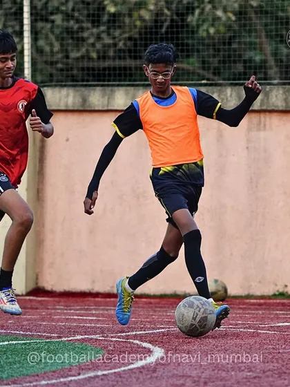 A player in an orange bib dribbles past an opponent during a training match at our Kalamboli center.