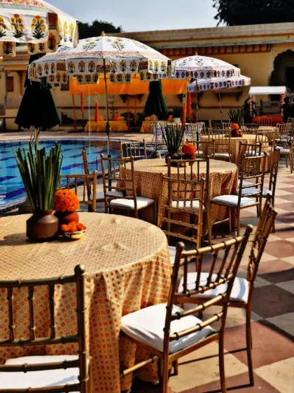 Poolside dining setup for a Haldi, with printed tablecloths and umbrellas that complement the festive, sunny theme.
