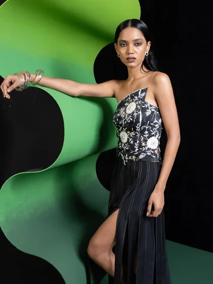 This look features a floral embroidered, one-shoulder corset paired with a pinstripe slit skirt. The styling combines romantic and structured elements for a contemporary feel.