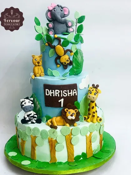 This three-tier jungle animal theme cake was made for a first birthday. It features adorable, hand-made fondant animals like a lion, giraffe, zebra, and monkey, all on a cake frosted with whipped cream.