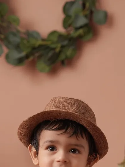 A charming, scholarly-themed portrait of a baby boy in a cute hat, with books and vintage props in the background.