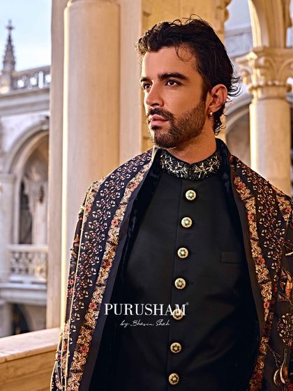 A close-up on the details. The embellished collar and custom buttons of this black bandhgala are set against the rich pattern of the shawl, creating a look of pure sovereignty.