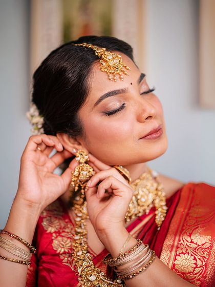 A bride getting ready, putting on her traditional temple jhumka earrings. This candid moment highlights the beauty of the jewellery and the anticipation of the ceremony.