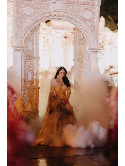 Raashi's grand entrance through an ornate archway, surrounded by smoke. This image is filled with drama and anticipation, making her bridal entry look like a scene from a royal film.
