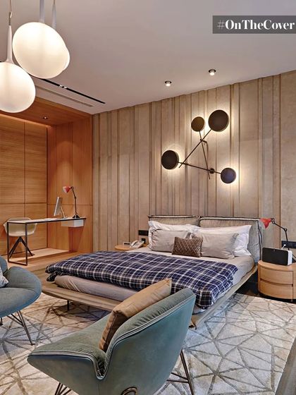 A cozy yet sophisticated bedroom design featuring a wood-paneled accent wall and modern art-like light fixtures. The space includes a compact work desk and comfortable seating, making it both functional and stylish.