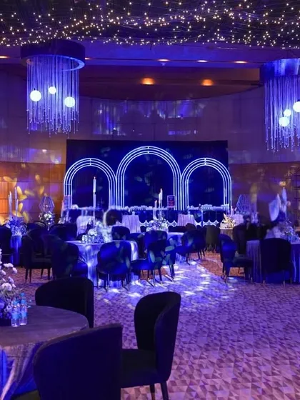 A wide view of the celestial-themed event, showing the dining area with floral centerpieces, the moon-themed lounge, and the neon-lit cocktail bar, all under a starry sky of fairy lights.