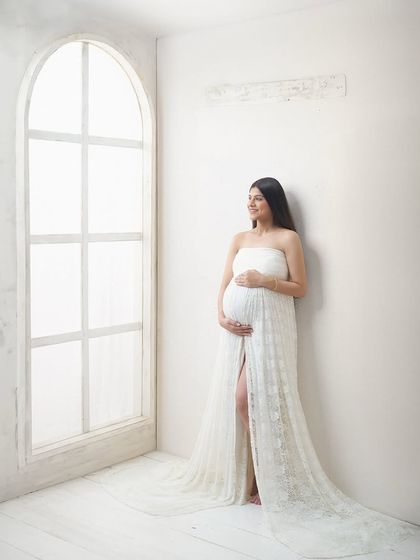A wide shot showing our bright and airy studio space. The minimalist white walls and large arched window provide a versatile and beautiful canvas for timeless maternity portraits.