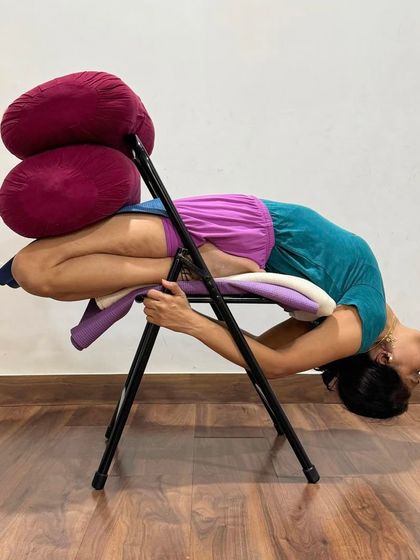 This is a supported backbend in Padmasana (Lotus Pose) on a chair. This variation combines a deep backbend with an intense hip opener, and the props make it a therapeutic posture for the spine and pelvis.