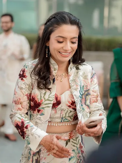 A candid moment of the bride checking her phone. Her soft makeup and braided hairstyle are perfect for a relaxed Mehendi.