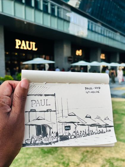 Holding up my finished pen sketch in front of the PAUL cafe in Hyderabad, capturing the architecture and the people enjoying their time.