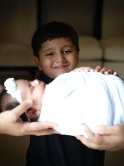 A creative and touching portrait showing a newborn being held by their parents' hands, with the proud older brother smiling in the background. This shot beautifully represents the whole family's love.