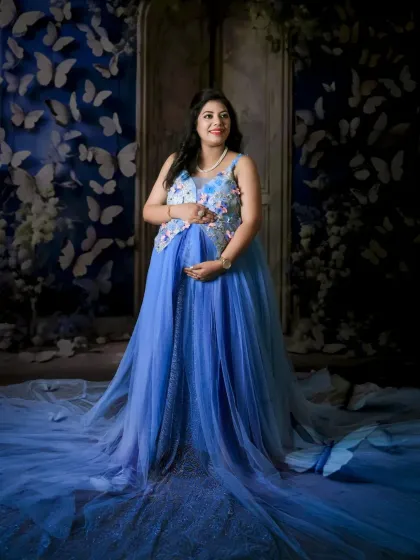 A fantasy-inspired solo portrait. The mom-to-be stands in a sea of blue butterflies against a magical, door-like backdrop, creating a truly unique and artistic image.