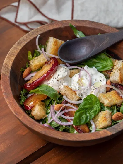 A Panzanella salad served in a rustic wooden bowl, featuring chunks of sourdough bread, roasted apples, and creamy burrata.