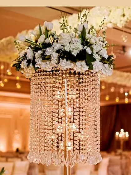 A luxurious centerpiece combining a tall crystal stand with a lush arrangement of white flowers, perfect for adding glamour to wedding reception tables.